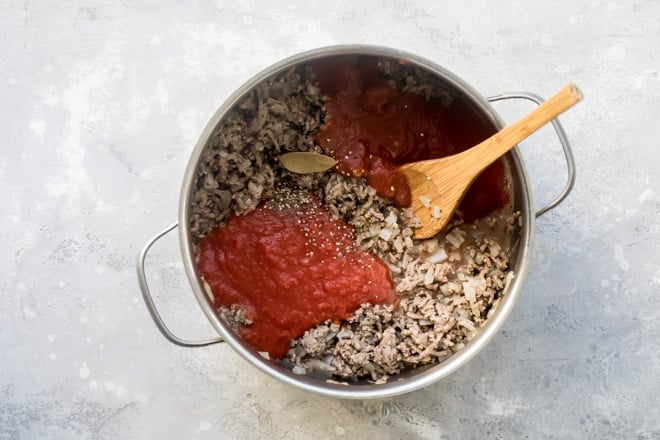 Homemade meat sauce ingredients in a silver pot with a wooden spoon.