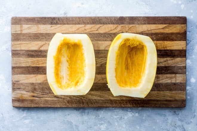 Two squash halves hollowed out on a wooden cutting board.
