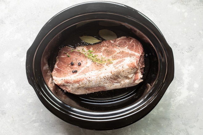 A pork roast in a crock pot with seasonings and spices.
