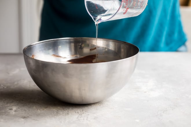 Chocolate glaze ingredients being added together in a silver bowl.