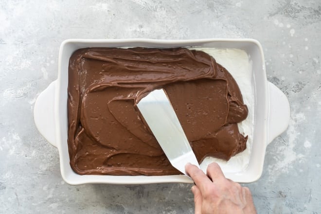 Chocolate layer of chocolate lasagna being added to a white baking dish.