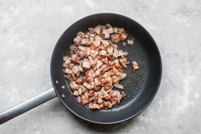 Bacon cooking in a black skillet.