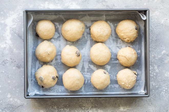 Pre-risen hot cross bun dough balls in a silver baking pan.
