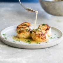Lemon butter sauce being drizzled onto pan-seared scallops.