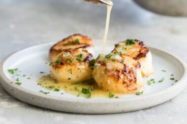 Lemon butter sauce being drizzled onto pan-seared scallops.