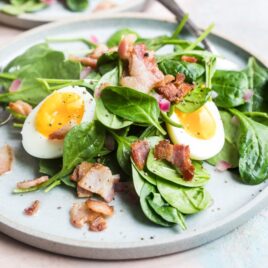 Spinach salad with bacon dressing on a white plate.
