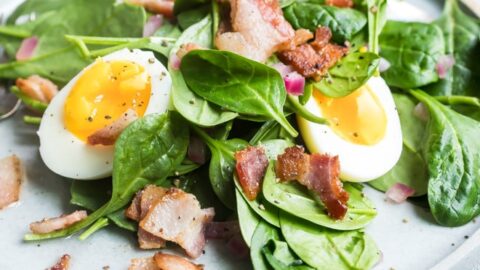 Spinach salad with bacon dressing on a white plate.