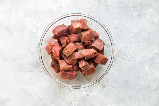 Uncooked steak tips in a clear bowl.