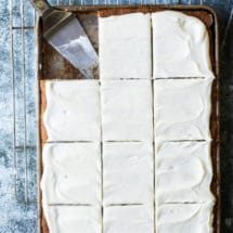 Cream cheese frosting spread over a jelly roll pan of banana bars (one square is missing).
