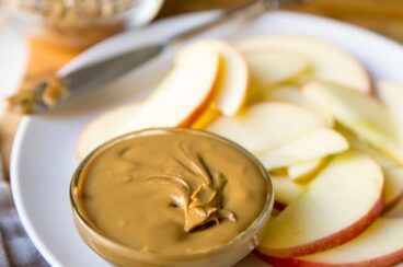 Homemade sunflower seed butter in a dish on a white plate with apple slices.