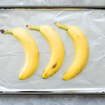 3 unpeeled yellow bananas on a foil-lined baking sheet.