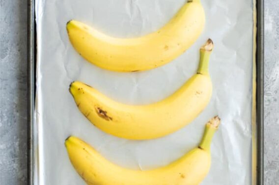 3 unpeeled yellow bananas on a foil-lined baking sheet.
