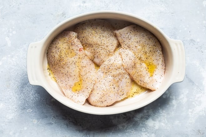 Uncooked chicken with seasoning in a baking dish.