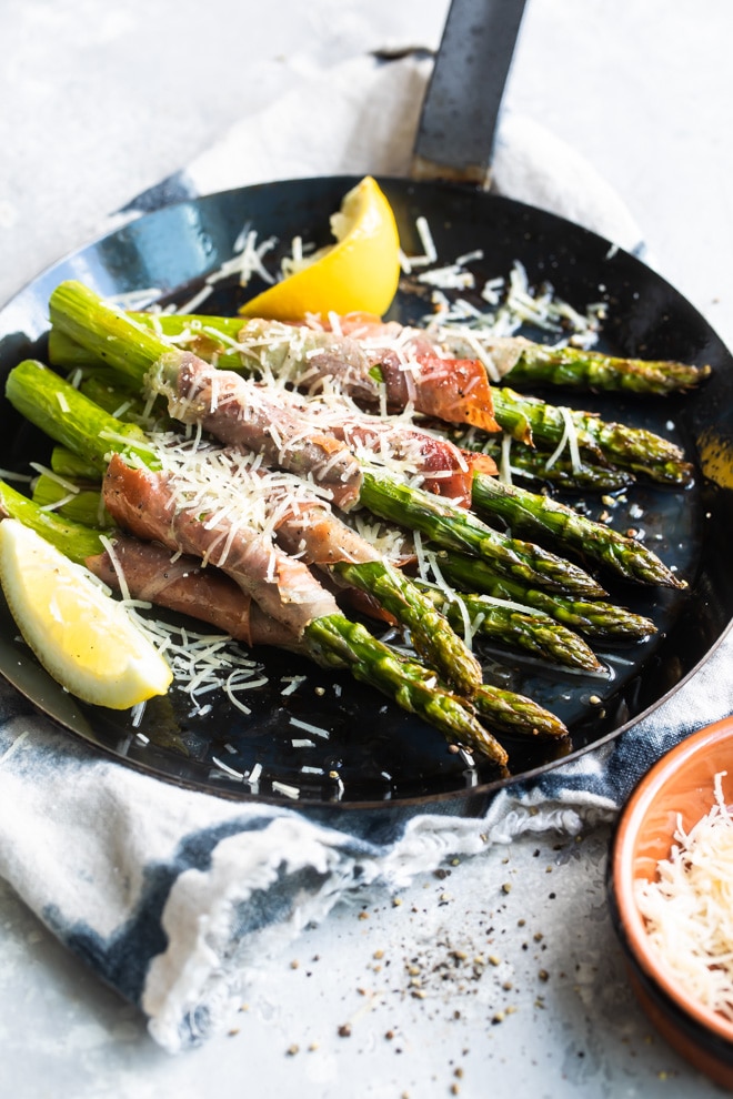 Prosciutto wrapped asparagus in a black pan.