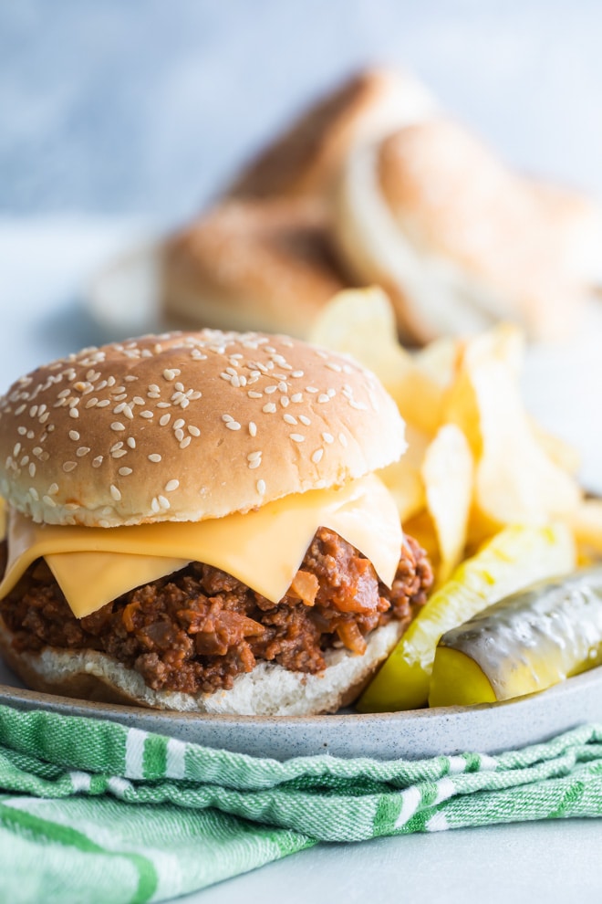 The best sloppy joes on a plate with pickles and chips.