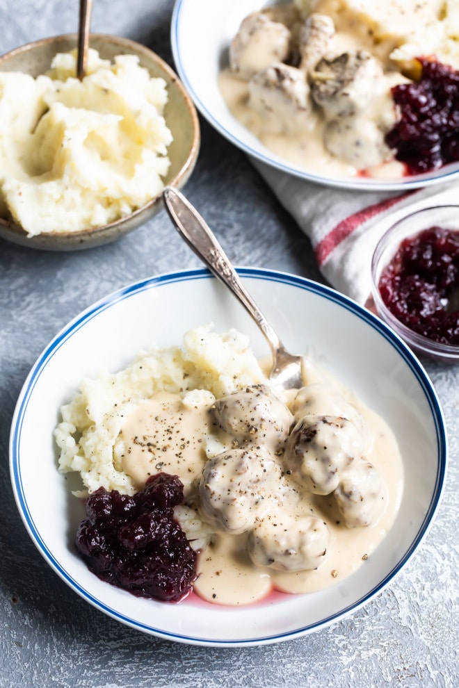 Swedish meatballs on plates with mashed potatoes, gravy, and cranberry sauce.