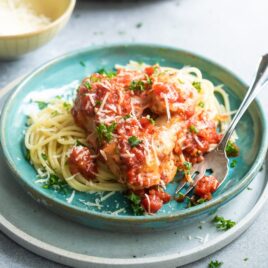 Chicken parmesan meatballs on spaghetti on a blue plate.
