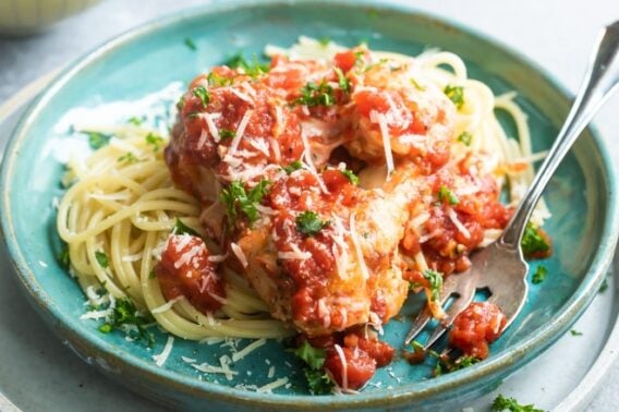 Chicken parmesan meatballs on spaghetti on a blue plate.