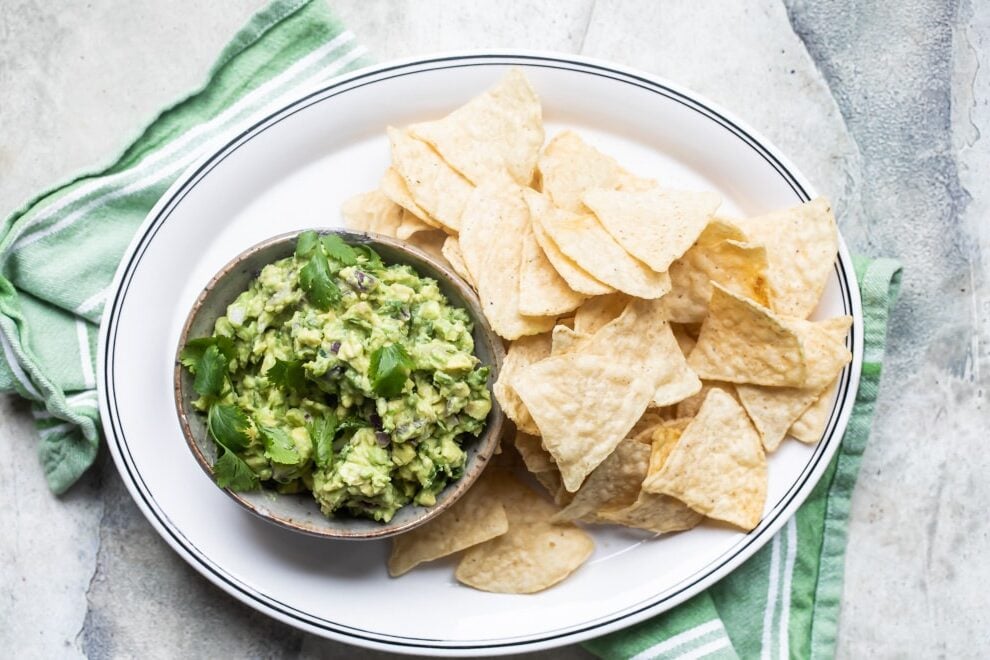 Chipotle guacamole in a serving dish on a white platter with tortilla chips.