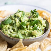 Chipotle guacamole in a bowl on a white plate with tortilla chips.