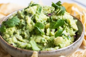Chipotle guacamole in a bowl on a white plate with tortilla chips.