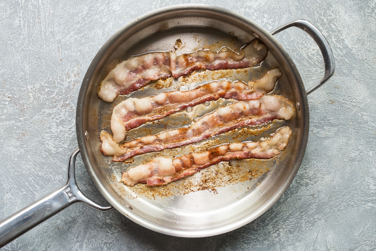 Bacon frying in a silver skillet.