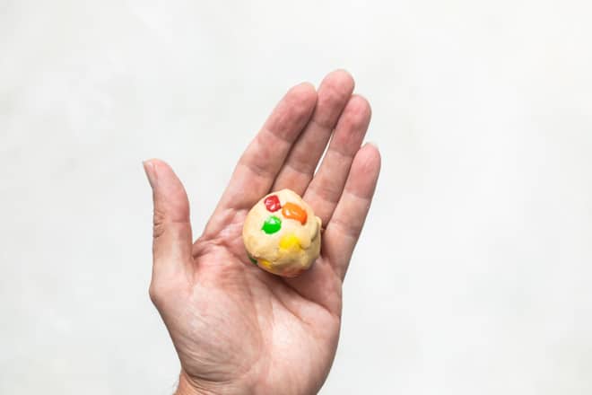 A single M&M cookie dough ball in the palm of somebody's hand.