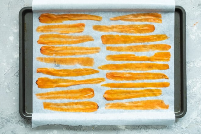Long carrot peels on a piece of parchment paper on a sheet pan.