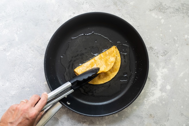 A corn tortilla being flipped on a black skillet.
