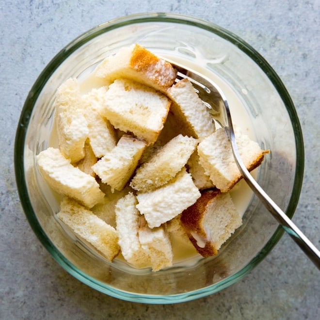 Chunks of white bread and cream in a clear bowl with a fork. 