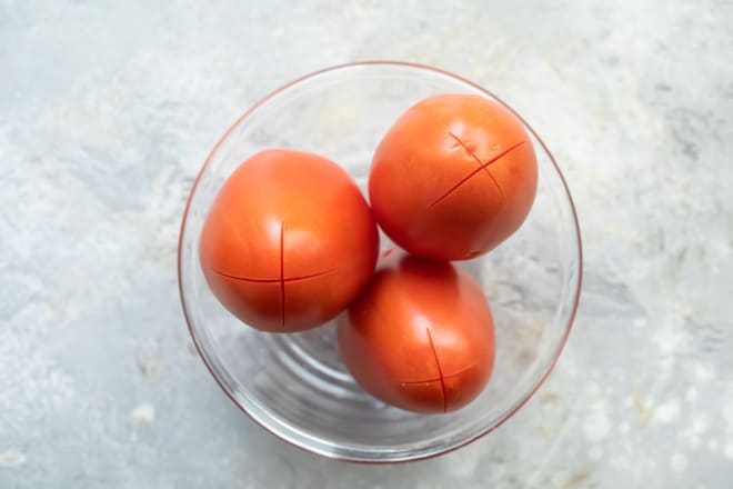 Three tomatoes in a clear glass bowl with x's cut into their tips.