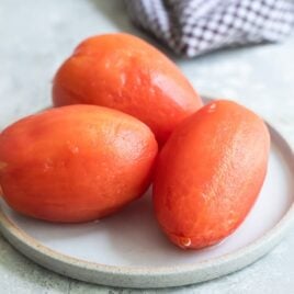 Three peeled tomatoes on a white plate.