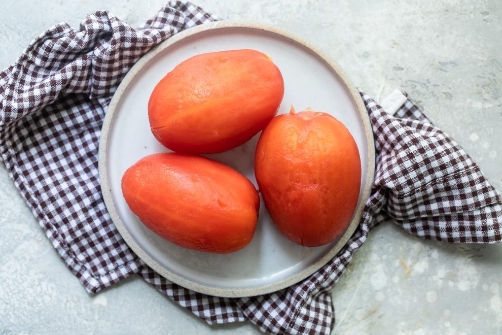 Three peeled tomatoes on a white plate.