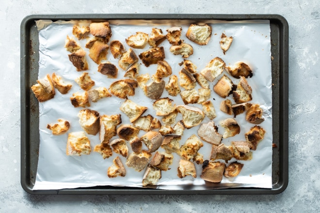 Ripped chunks of bread toasted on a baking sheet lined with tin foil.