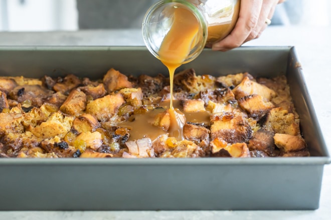 Caramel sauce being poured onto baked bread pudding.