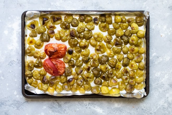 A halved tomato and halved green chilies baked on a baking sheet lined with tin foil.