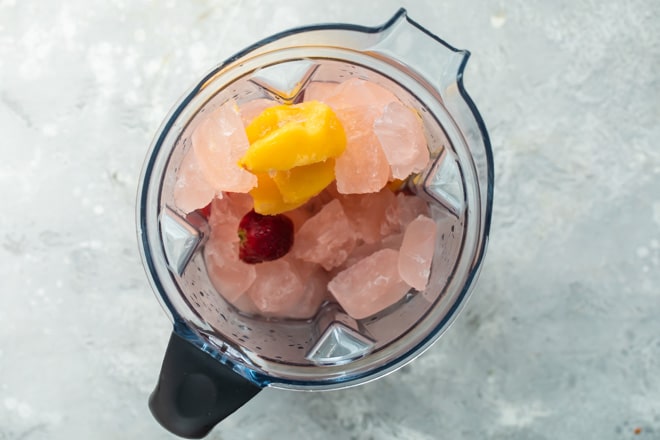 Frozen rose cubes and chunks of frozen fruit in a blender.