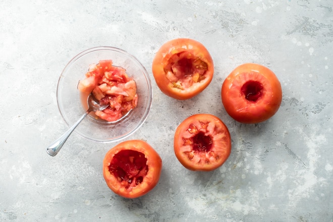 Four tomatoes being hollowed out.
