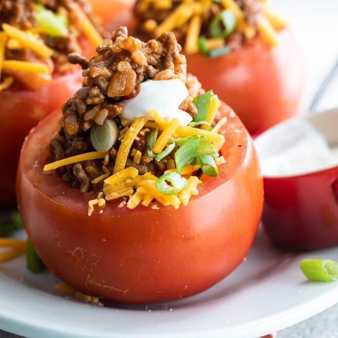 Four taco stuffed tomatoes on a white platter.