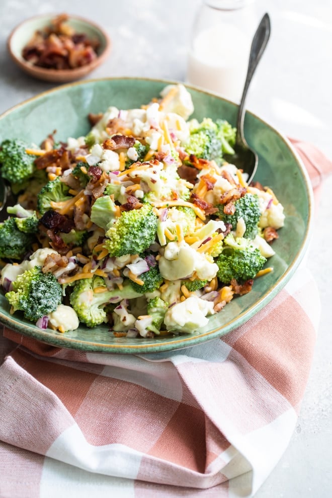 Broccoli salad with bacon and cheese in a green bowl with a spoon.