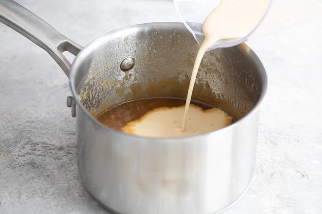 Evaporated milk being poured into a metal saucepan with other caramel sauce ingredients.