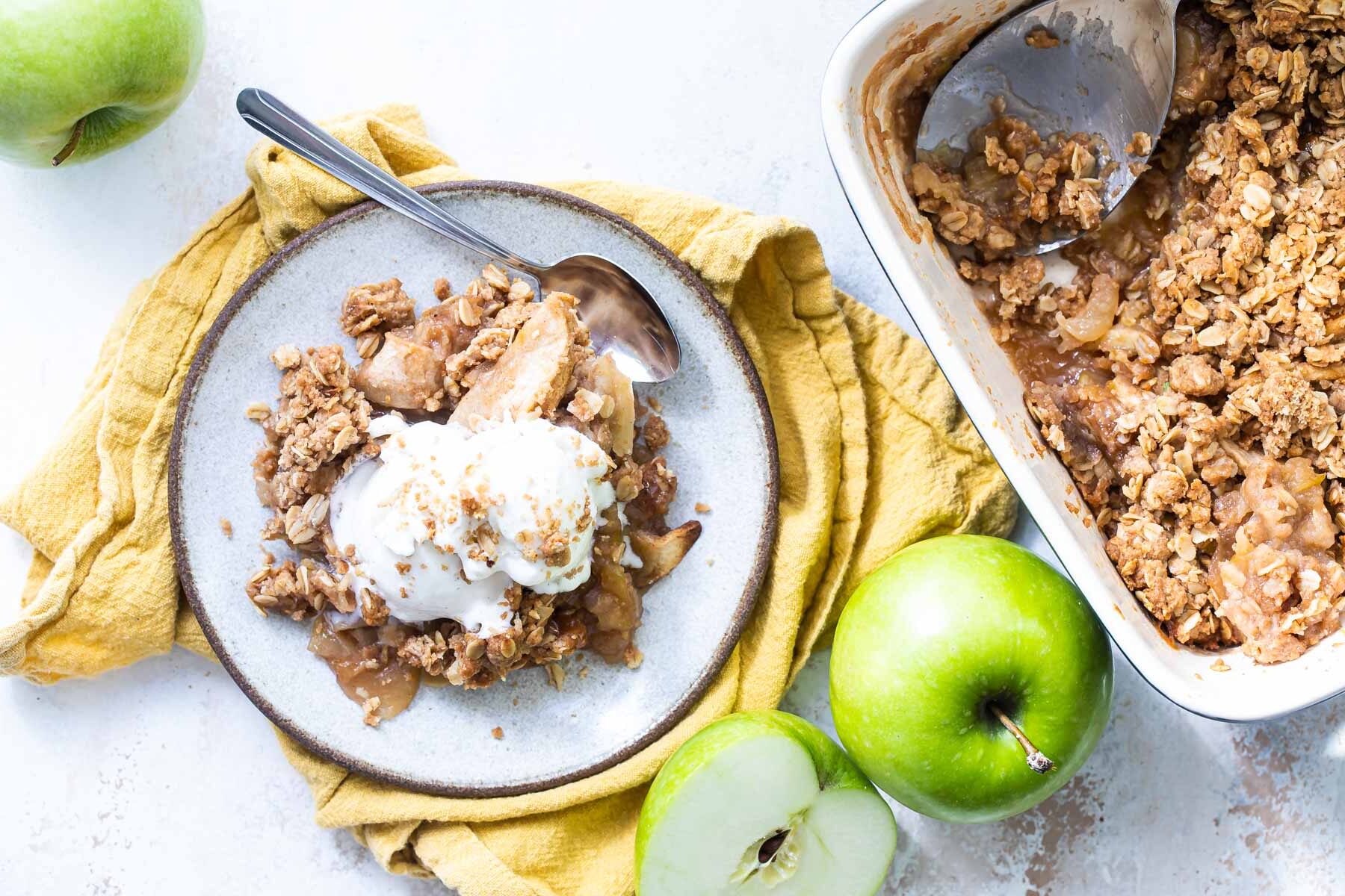 Apple crisp on a plate with a scoop of ice cream on top.