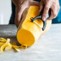 Peeling butternut squash with a vegetable peeler.