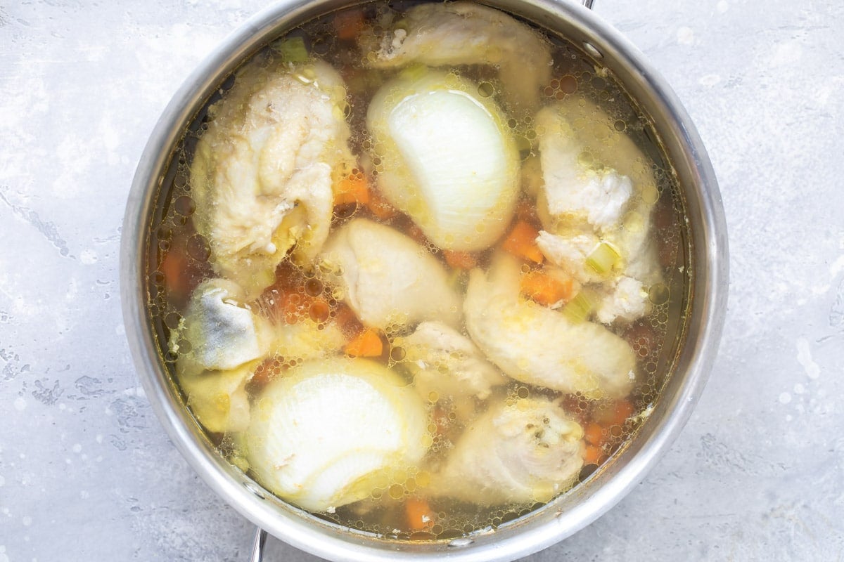 Chicken broth ingredients in water in a silver pot.