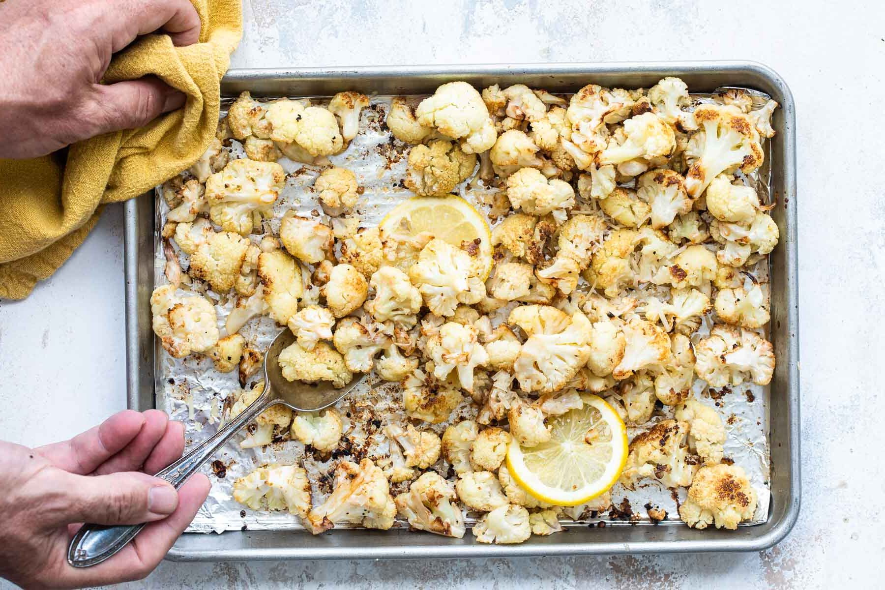 Someone scooping a spoonful of roasted cauliflower off of a baking sheet.