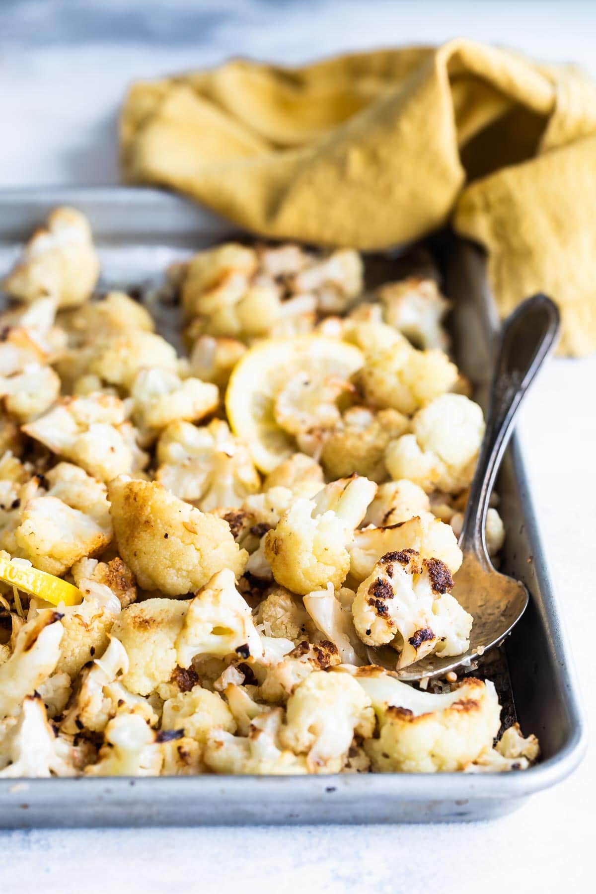 Roasted cauliflower on a baking sheet with a spoon resting in it.