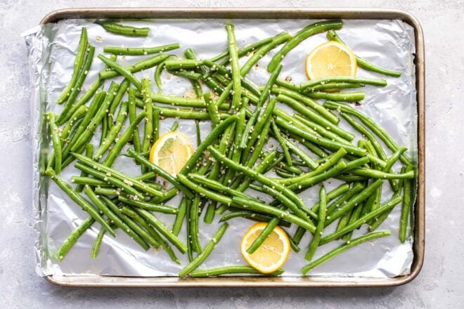 Green beans on a baking sheet coated in oil and seasonings before being roasted.