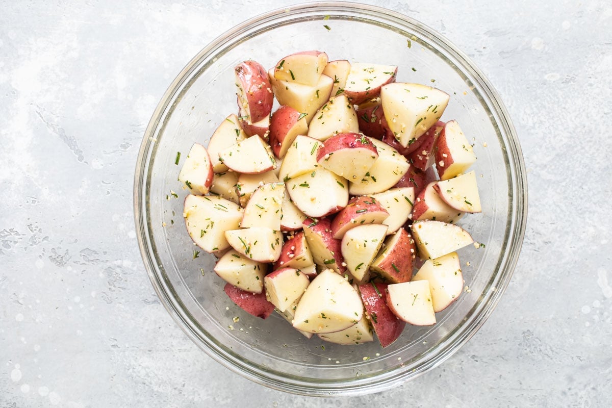Red potatoes with seasoning in a clear bowl.