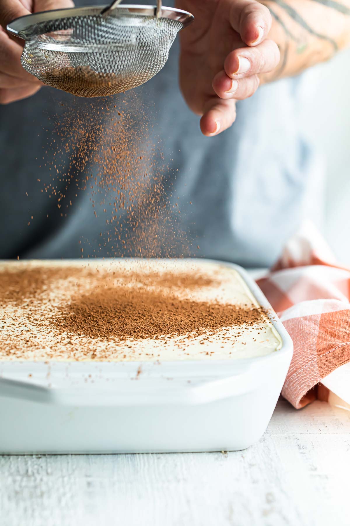 Tiramisu being dusted with cocoa powder.