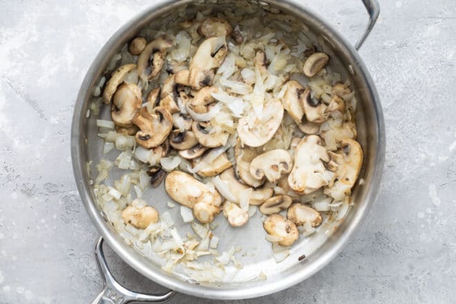Mushrooms and onions cooking in a skillet.